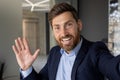 Close-up portrait of a smiling and successful young businessman in a suit standing in the office, waving and greeting Royalty Free Stock Photo