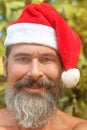 Close-up portrait of smiling, well tanned, bearded caucasian man in a Santa Claus hat standing in front of cacti on the