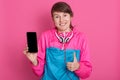 Close up portrait of smiling woman holding phone with blank screen and showing ok sign with her thu, girl has ponytail, wearing Royalty Free Stock Photo