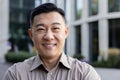 Close-up portrait of a smiling young Asian man in a brown shirt standing on a city street and looking confidently into Royalty Free Stock Photo