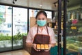 Close up portrait smiling young Asian woman in a beige shirt with an apron, she is wearing a face mask holding a butter cake pack Royalty Free Stock Photo