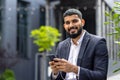 Close-up portrait of a smiling young Muslim businessman in a suit standing outside an office building wearing headphones Royalty Free Stock Photo