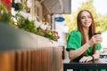Close-up portrait of smiling young woman holding cup with tasty coffee sitting at table in outdoor cafe terrace in Royalty Free Stock Photo