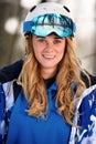 Close up portrait of snowboarder woman at ski resort wearing helmet and goggles with reflection of forest in mountains Royalty Free Stock Photo