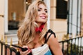 Close-up portrait of spectacular woman with blonde shiny hair looking up and laughing near restaurant. Cheerful lady