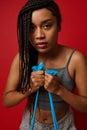Close-up portrait of a strong African woman, female athlete with stylish dreadlocks, exercising with resistance band against red
