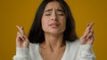 Close up portrait in studio yellow background Indian ethnic woman girl lady female makes wish crosses fingers for good Royalty Free Stock Photo