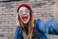 Close-up portrait of stunning blonde lady in denim jacket making selfie with smile. Photo of joyful