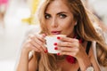 Close-up portrait of stunning blue-eyed lady chilling in cafe and drinking hot coffee. Photo of refined girl with red