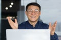 Close up portrait of successful asian man inside office, businessman using laptop at work smiling and looking at camera Royalty Free Stock Photo