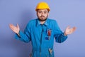 Close up portrait surprised bearded builder dresses helmet and uniform, spreading his hands to sides, squeezing his shoulders, Royalty Free Stock Photo