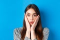 Close-up portrait of surprised cute woman holding hands on cheeks and gasping, stare at camera shocked, standing against Royalty Free Stock Photo