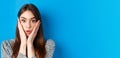 Close-up portrait of surprised cute woman holding hands on cheeks and gasping, stare at camera shocked, standing against Royalty Free Stock Photo