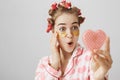 Close-up portrait of surprised or impressed young girl in hair-curlers and eye patch mask looking at heart-shaped mirror Royalty Free Stock Photo