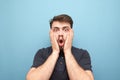 Close-up portrait of a surprised man that took a hand on the face of fear,looks emotionally into the camera on a blue background.