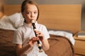 Close-up portrait of talented adorable little girl playing flute sitting on bed in bedroom, looking at camera. Royalty Free Stock Photo