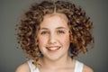 Close-up portrait. Teen girl with curly hair smiles beautifully. The vzgyad directs directly into the frame. Gray background.