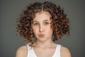 Close-up portrait. A teenage girl with curly hair curled her lips into a tube. The vzgyad directs directly into the frame. Gray