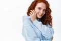 Close up portrait of tender and beautiful redhead girl tuck her curly hair behind ear and smiling lovely at camera Royalty Free Stock Photo