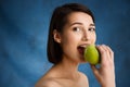 Close up portrait of tender young girl biting apple over blue background Royalty Free Stock Photo