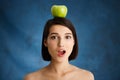 Close up portrait of tender young girl holding apple on her head over blue background Royalty Free Stock Photo
