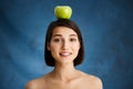 Close up portrait of tender young girl holding apple on her head over blue background Royalty Free Stock Photo