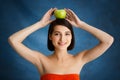 Close up portrait of tender young girl holding apple on her head over blue background Royalty Free Stock Photo