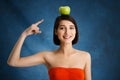 Close up portrait of tender young girl pointing with finger at apple on her head over blue background Royalty Free Stock Photo