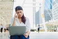 Close up portrait thoughtful young Asian woman in white shirt sitting on floor wondering or thinking about something with laptop Royalty Free Stock Photo