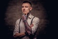 Close-up portrait of a young old-fashioned tattooed guy wearing white shirt and suspenders. Isolated on dark background. Royalty Free Stock Photo