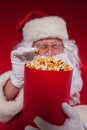 Close-up portrait Traditional Santa Claus watching TV, eating popcorn. Christmas. Red background. emotions. fear