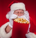 Close-up portrait Traditional Santa Claus watching TV, eating popcorn. Christmas. Red background. emotions. fear