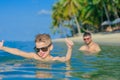 Close-up portrait in tropical water: seven years old cutest blond boy lying on the water surface, held up thumbs and show tongue.