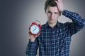 Close-up portrait of a troubled young man holding alarm clock isolated over white background. Royalty Free Stock Photo