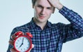 Close-up portrait of a troubled young man holding alarm clock isolated over white background. Royalty Free Stock Photo