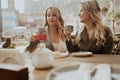 Close-up portrait of two female friends in strict suits laughing drinking coffee and wine on the terrace outside at Royalty Free Stock Photo