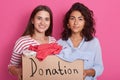 Close up portrait of two girls volunteering, women holding paper box with clothes for poor people, friends making donation,