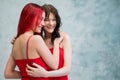 A close-up portrait of two tenderly embracing women dressed in identical red dresses. Lesbian intimacy. Royalty Free Stock Photo