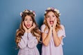 Close-up portrait of two winsome ladies posing on blue background with surprised face expression. Indoor photo of girls Royalty Free Stock Photo