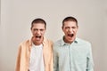 Close up portrait of two young angry twin brothers shouting and looking at camera while posing together isolated over