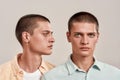 Close up portrait of two young caucasian twin brothers posing together in studio, standing isolated over beige