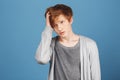 Close up portrait of unhappy young charming ginger male student in casual clothes holding hair with hand, looking aside Royalty Free Stock Photo