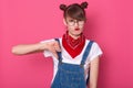 Close up portrait of unimpressed disliking attractive female student dresses denim overall, white t shirt and red bandana, showing Royalty Free Stock Photo