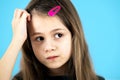 Close up portrait of upset and pensive little girl with cute pink hairpin on blue background