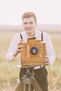 The close-up portrait of the vintage dressed groom taking photos using the wooden old camera at the background of the Royalty Free Stock Photo