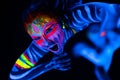 Close-up Portrait of Wild and frantic Young naked bodyarted woman in blue glowing ultraviolet paint and Yellow eye