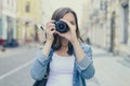 Close up portrait of woman in casual clothes taking photo on her digital camera. Lens is in focus, blurred city street is on the b Royalty Free Stock Photo