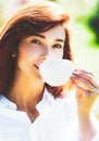 Close up portrait of a woman holding a hot coffee cup outdoors on the spring background. Red head girl drinking coffe. Royalty Free Stock Photo