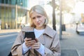 Close up portrait of woman looking sceptical at her mobile phone, standing on street, frowning and standing perplexed