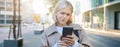 Close up portrait of woman looking sceptical at her mobile phone, standing on street, frowning and standing perplexed